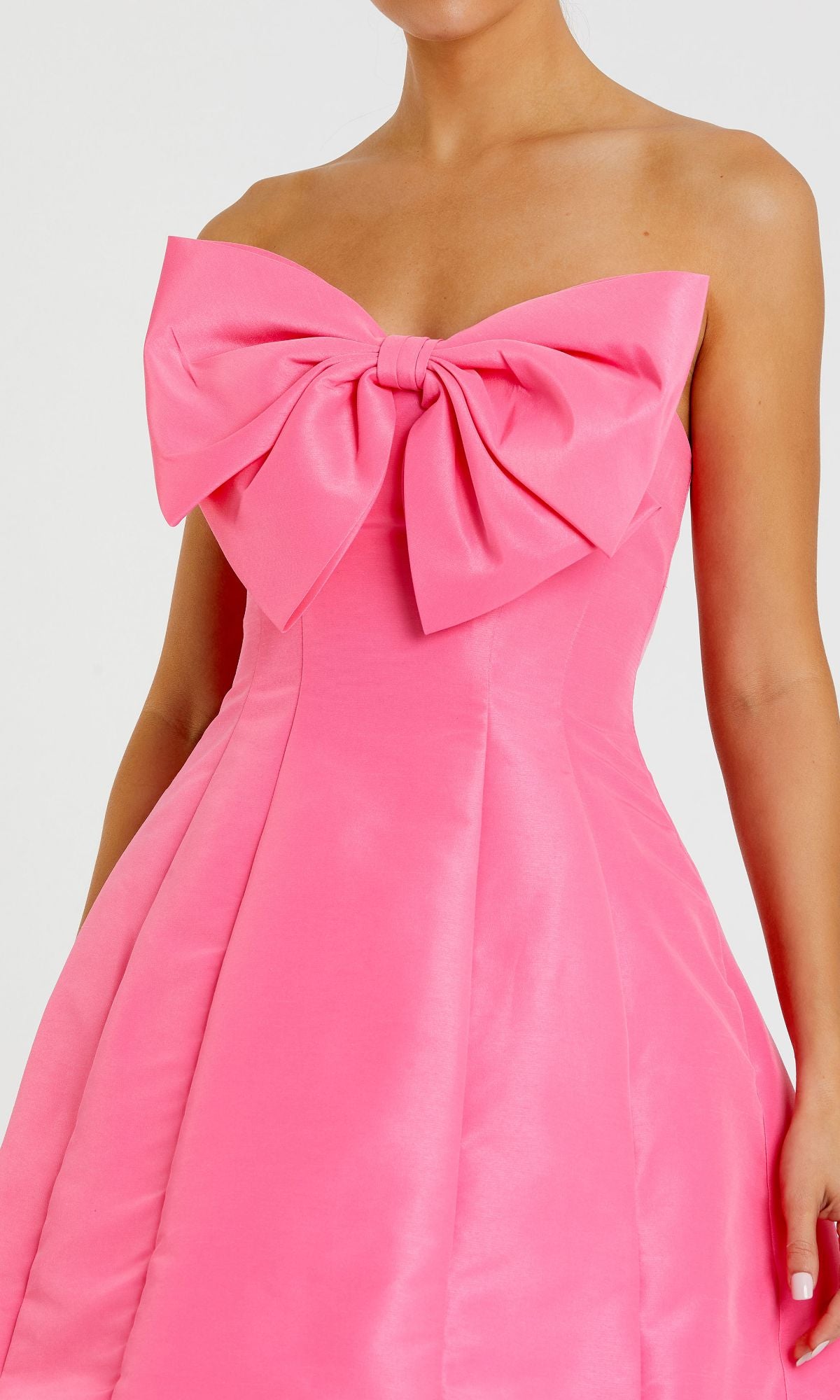 A woman models the Mac Duggal 49210 Strapless Short Bow Party Dress in bright pink, featuring a large chest bow, against a plain background.